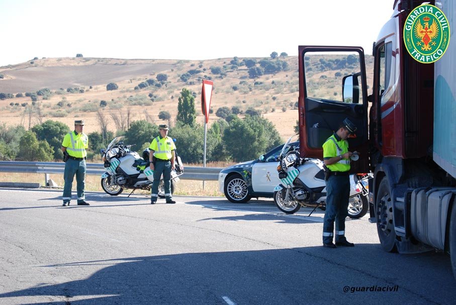 Agentes de la Guardia Civil de Tráfico realizando un control a un camión en carretera, con motocicletas y coche patrulla