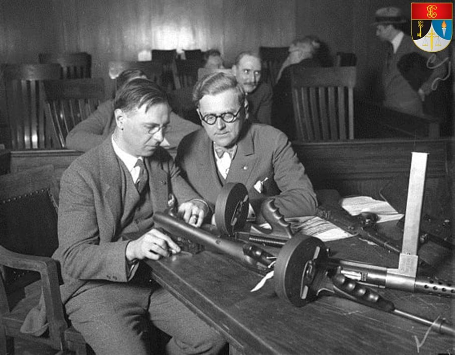 Fotografía histórica de dos expertos examinando subfusiles en una sala de vistas a principios del siglo XX